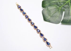 Détail d'un bracelet doré avec cristaux bleus en goutte et petits strass sur fond blanc