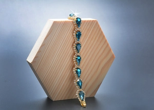 Détail d'un bracelet doré avec cristal bleu en forme de goutte sur un support en bois