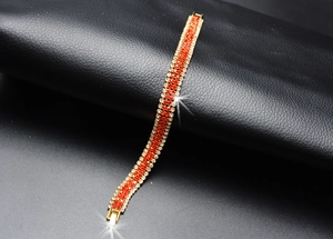 Macro shot of gold-plated bracelet with red and clear rhinestones on black leather