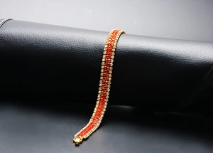 Detailed shot of golden bracelet with red and white inlaid crystals on black leather