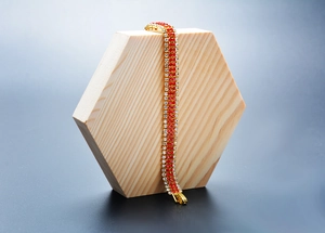 Detailed shot of a gold-plated bracelet with red and clear rhinestones on a wooden block