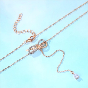 Rose gold bow necklace with sparkling crystals and drop pendant on light blue background