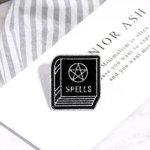 Detail of black enamel Spells book pin with a pentagram and silver metal edges