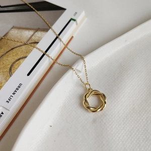 Detail shot of a golden twisted wreath pendant on a white ceramic tray with lifestyle props