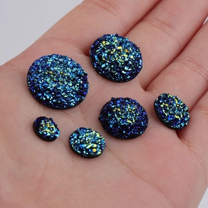 Close-up of sparkling dark blue and green druzy resin cabochons held in hand for scale