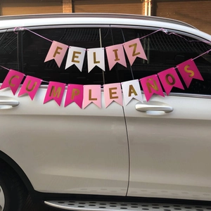 Close-up of pink and white Feliz Cumpleaños birthday banner hung on a white SUV