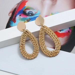 Détail de boucles d'oreilles en rotin tressé en forme de goutte avec clous dorés