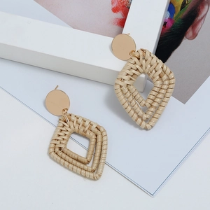 Détail macro de boucles d'oreilles géométriques en rotin tressé avec clous en métal doré
