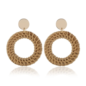 Détail de boucles d'oreilles en rotin tressé à la main avec clous dorés et reflets nets