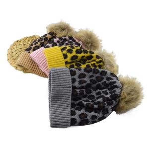 Detail of four leopard print knit beanies with large faux fur pom poms in various colors