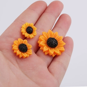 Three yellow resin sunflower DIY craft charms for hair accessories shown in a hand