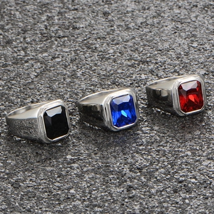 Detailed close-up of square cut gemstone rings in black, blue, and red on stone surface