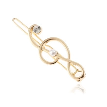 Close-up of golden treble clef hair clip featuring a white pearl and sparkling rhinestone