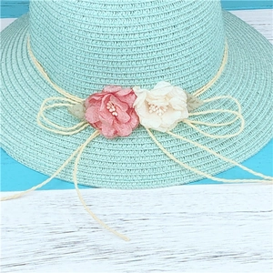 Chapeau de soleil en paille vert menthe avec fleurs en tissu sur fond en bois bleu clair