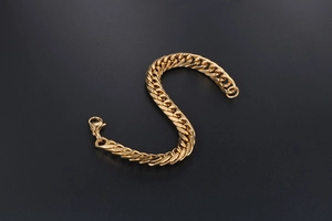 Detailed view of thick golden Cuban link bracelet with lobster clasp on black background
