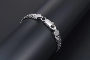 Detail of silver stainless steel chain bracelet draped over a dark minimalist pedestal