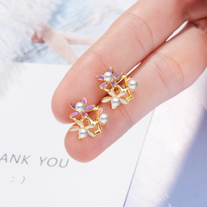 Floral stud earrings with purple and white petals and pearl center held by hand