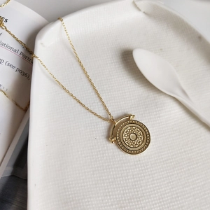 Detailed macro view of a gold-plated circular sunburst medallion on a delicate link chain