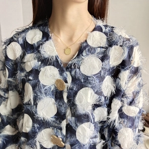 Detailed shot of an embossed gold coin pendant necklace worn with a polka dot jacket