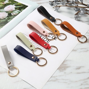 Minimalist leather keychains in eight assorted colors with golden metal rings on white marble