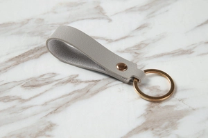 Close-up of grey leather loop keychain with gold metal rivet on marble background