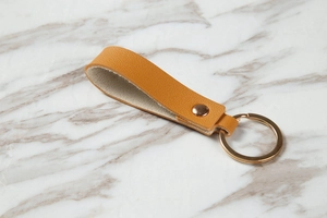 Close-up of premium brown leather keychain with golden metal ring on marble background