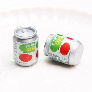 Close-up of miniature soda can charms with apple motifs on a white textured plate