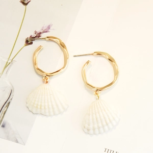 Detail of bohemian gold irregular hoop earrings with white shell pendants on a white paper