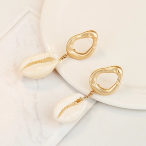 Close-up of golden wire-wrapped seashell earrings on a white ceramic display