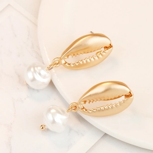 Macro detail of matte gold shell earrings with natural white baroque pearl pendants