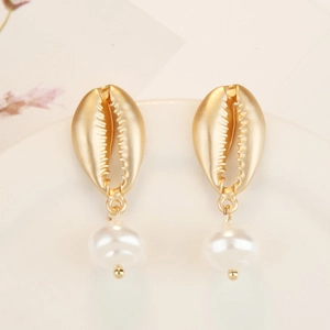 Detail of bohemian shell and pearl earrings on a ceramic dish with dried flowers