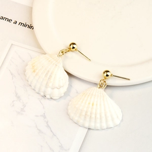 Macro shot of natural white shell earrings with gold metal studs on a marble surface