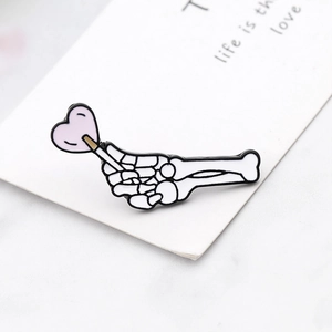 Macro detail of skeleton hand enamel brooch holding pink heart lollipop on a marble surface