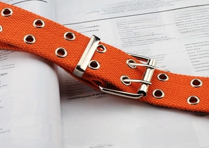 Close-up of orange double-eyelet canvas belt with silver metal buckle on a magazine
