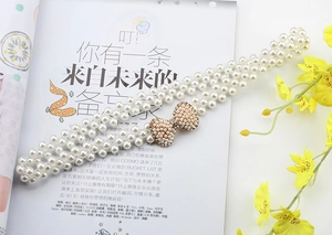 Detail of elegant triple-row pearl belt with a sparkling rhinestone bow buckle on a magazine
