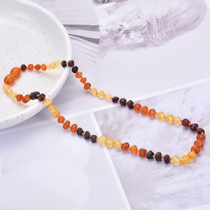 Natural Baltic amber baby necklace with multi-color beads on a white ceramic plate