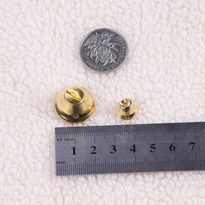 Size comparison of gold Christmas bells with a ruler and coin on a beige plush surface