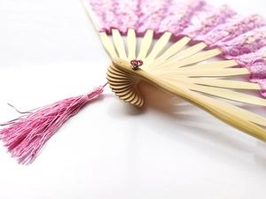 Close-up of pink lace hand fan with bamboo ribs and matching decorative tassel detail