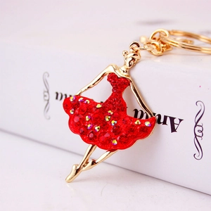 Golden ballet girl keychain with red rhinestone dress displayed on an elegant white book