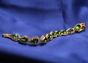 Détail d'un bracelet doré orné de grandes pierres vertes en poire et de cristaux