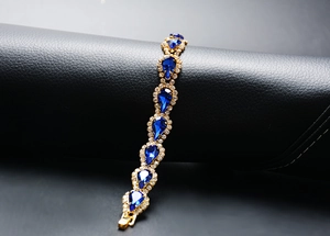 Vue détaillée d'un bracelet doré avec pierres bleues en forme de goutte et fermoir pliant
