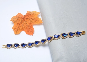 Détail du bracelet doré avec des pierres bleues en goutte d'eau et une feuille d'érable