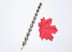 Détail d'un bracelet doré avec cristal goutte bleu profond et strass brillants