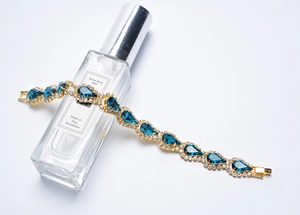 Détail d'un bracelet doré avec cristaux bleus en goutte sur un flacon de parfum