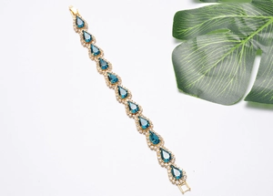 Gros plan d'un bracelet doré avec cristaux goutte bleus et petits diamants sur fond blanc