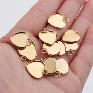 Golden heart-shaped stainless steel pendant charms held in hand for size comparison