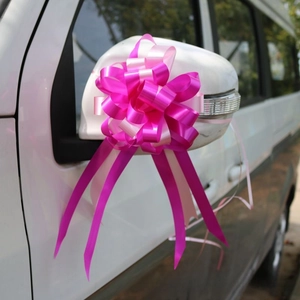 Pink and purple decorative ribbon bow flower with long streamers attached to a car mirror