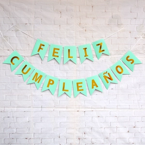 Detail of Spanish Feliz Cumpleaños mint green banner with gold foil letters on white brick wall