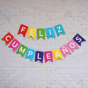 Colorful Feliz Cumpleaños Spanish birthday banner with glitter flags on a white brick wall