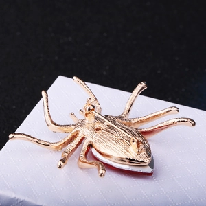 Elegant gold spider brooch with sparkling red crystal inlay on a minimalist background